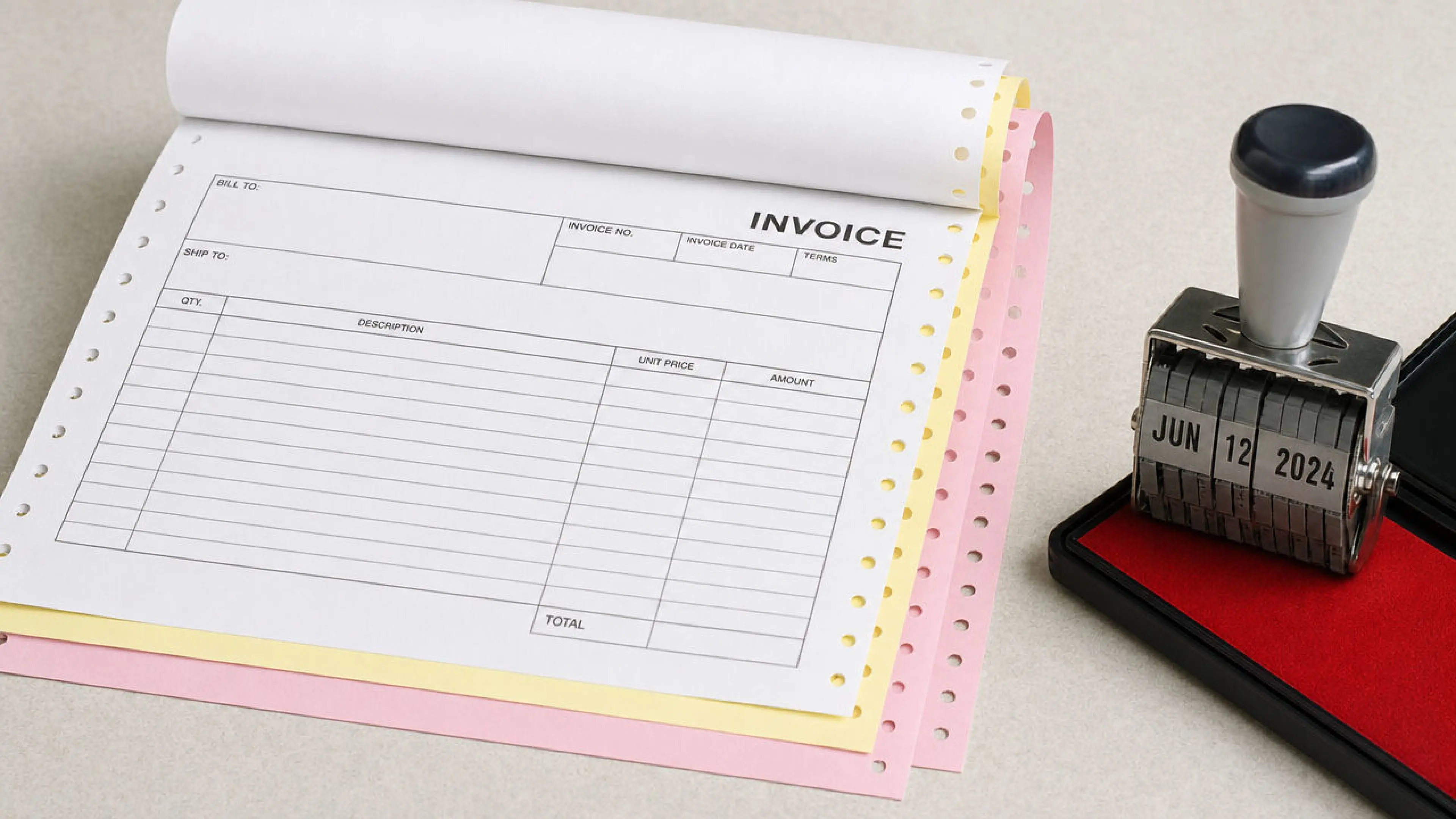A fluorescent accounts desk with a fanned triplicate invoice roll, perforated edges, a date stamp, and a black ballpoint.